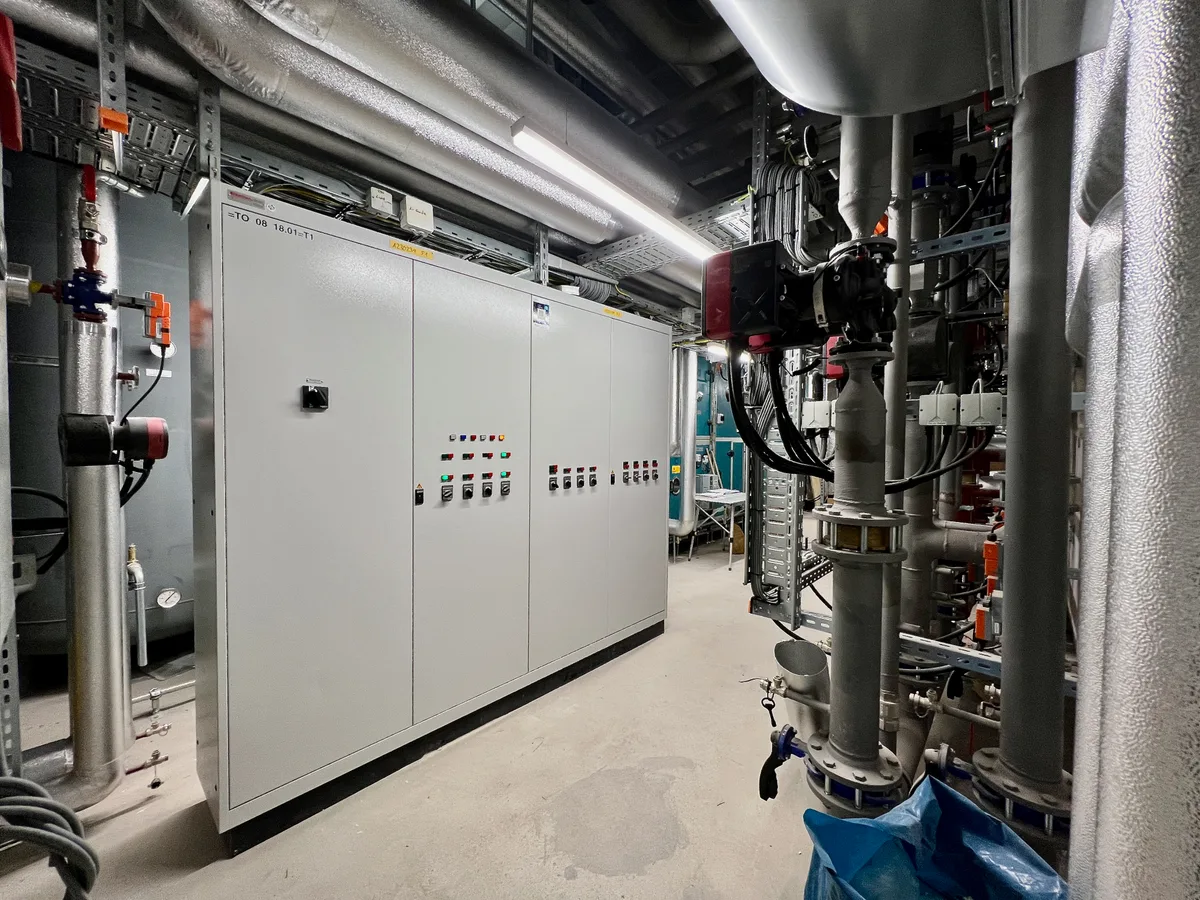 Man sieht einen grossen grauen Kasten in einem Kellerraum, an dem einige Leuchtknöpfe und Schalter angebracht sind.